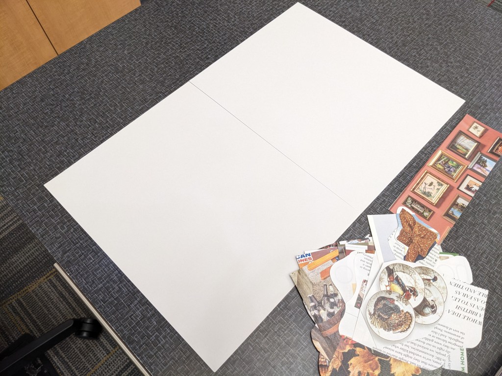 Two pieces of cardstock are taped together on a desk, with a handful of magazine clippings to the side.