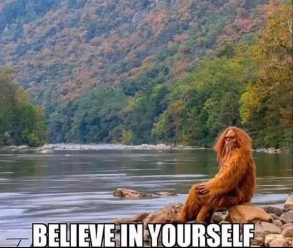 An image of Bigfoot sitting on a rock at the edge of a lake, with autumnal trees lining the backdrop. The meme caption "Believe in yourself" lines the bottom of the image in Impact font.